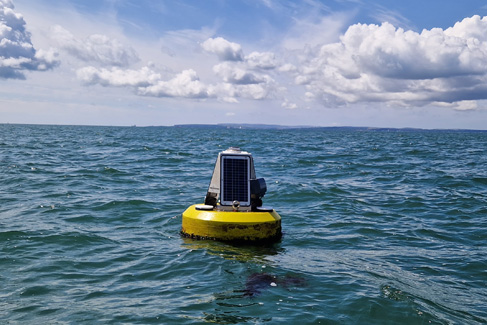 A bright yellow data buoy with solar panel mounted floating in the sea